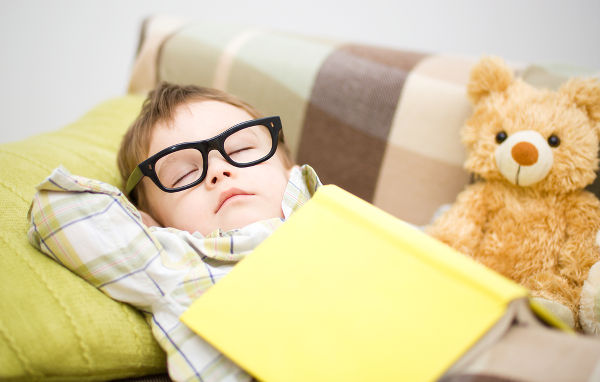 boy is sleeping in front of his teddy bears wearing glasses
