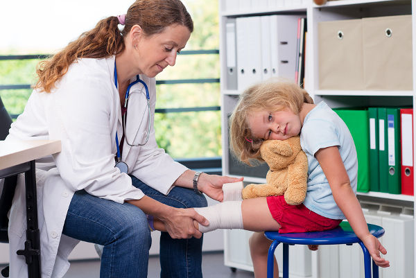 female pediatrician in white lab coat bandaging the leg of a little girl