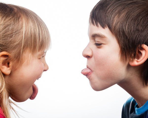 Close-up shot of boy and girl sticking out tongues to each other on white background. Children are half-siblings.