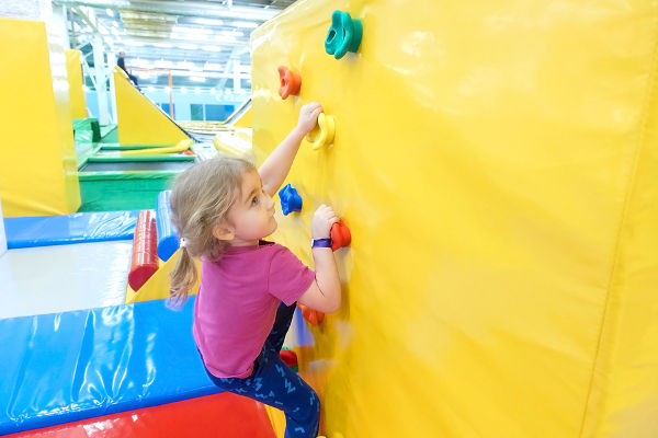Little Girl Climbing a Rock Wall Indoor. Children's Entertainment Sports Soft Ground.
