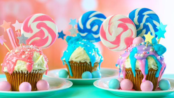 Three pink and blue theme colorful novelty cupcakes decorated with candy and large heart shaped lollipops for children's, teen's birthday or holiday celebrations.
