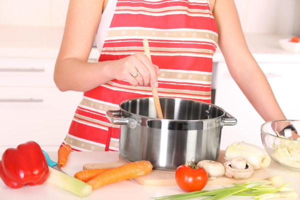 A picture of a housewife preparing soup in a pot in the kitchen