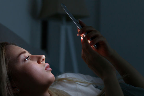Woman addicted to the smartphone connected 24/7 to internet, lying on bed and using smart phone at late night.