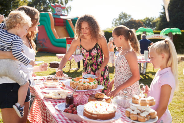 Children Serving On Cake Stall At Busy Summer Garden Fete
