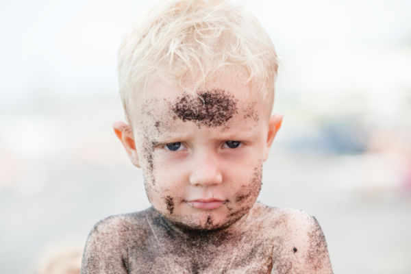 little blonde boy covered in sand at the beach
