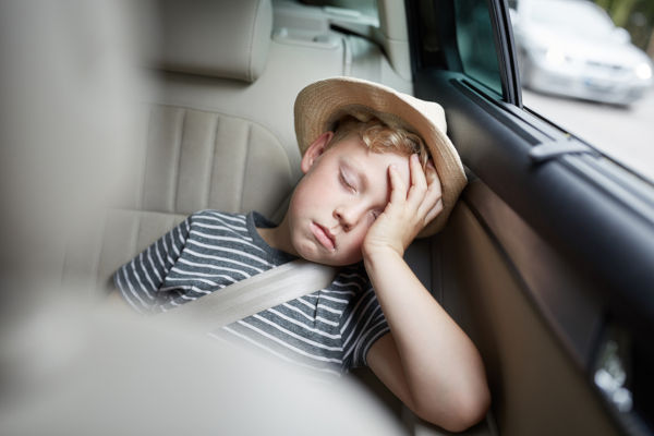 Boy with hat is sleeping on the back seat in the car on the road trip on vacation