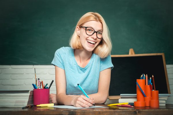 Female teacher sat at desk in front of blackboard
