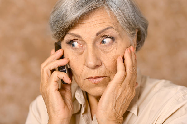 Portrait of worried elderly woman speaking on mobile against brown background