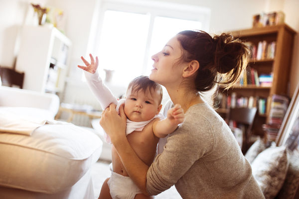 Cute little baby girl getting dressed by her mother on a carpet in a living room.