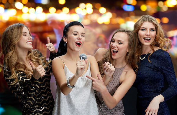 three women in evening dresses with microphone singing karaoke