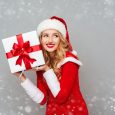 Smiling excited Woman in red santa claus outfit holding christmas gift