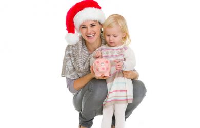 Happy mother in Christmas hat and baby girl putting coin into piggy bank