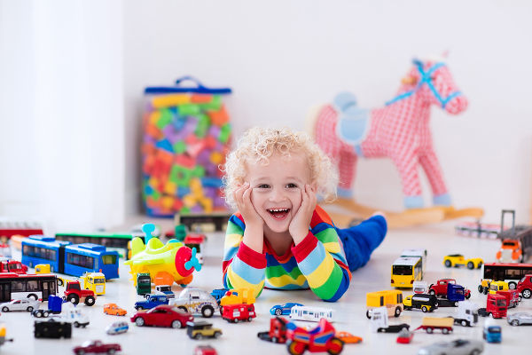 Funny curly toddler boy playing with his model car collection on the floor