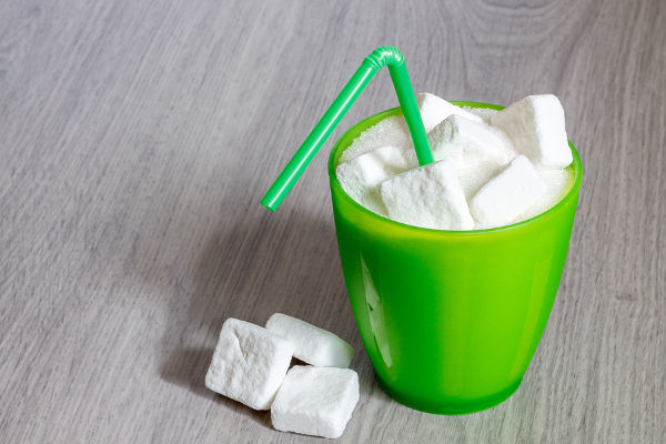 Green plastic glass with straw full of sugar and sugar cubes