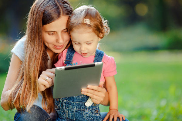 Beautiful mother and kid girl playing at tablet pc outdoors in fall