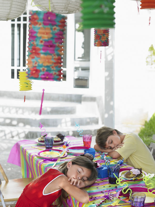 Boy and girl sleeping at outdoor table after birthday party
