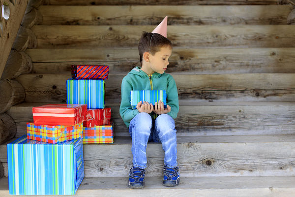 child sits alone surrounded by gifts and sad looking an empty place next to him