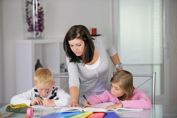 Portrait of young woman helping a boy and a girl in doing homework