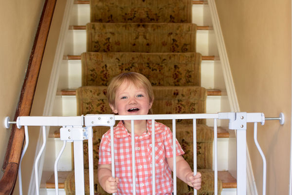 Adorable toddler boy standing on steps behind baby gate