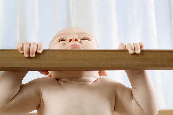 Baby boy holding himself up in wooden cot at home