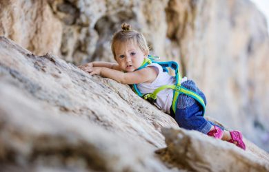 Little girl in safety harness climbing up cliff