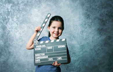 Little girl with a clapperboard on grey background