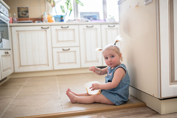 Girl with pigtails eating ice cream from a jar sitting on the floor in the kitchen