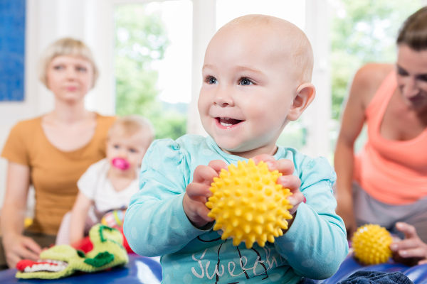 Babies with pacifier in toddler group playing with toys in baby course