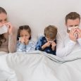 Sick parents ans children lying in a bed and blowing noses in napkins