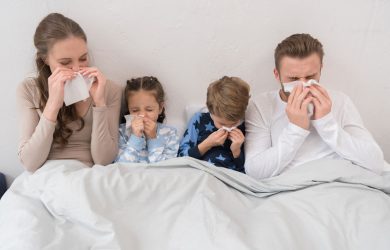 Sick parents ans children lying in a bed and blowing noses in napkins