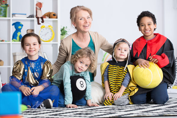 Dressed up children in colorful costumes and happy kindergarten teacher