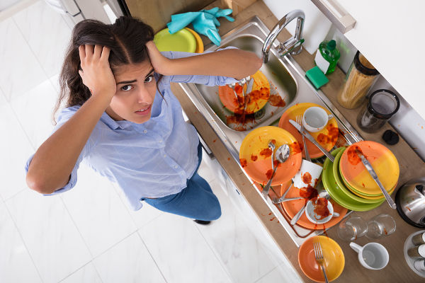 Frustrated Young Woman Standing Near Messy Utensils On Countertop In Kitchen