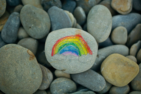 Close-up of painted rainbow on stone on pebble beach.