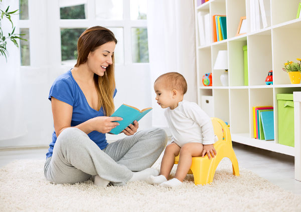 Cute baby sitting on bedpan and listening kid story with mom