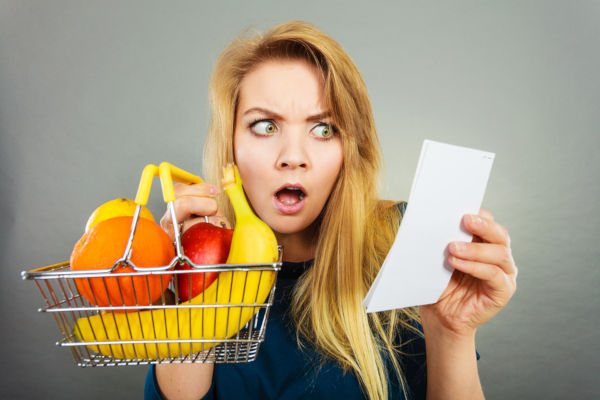 Shocked Woman Holding Shopping Basket With Fruits Looking At Bil