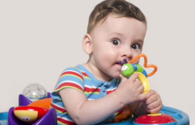 Cute baby boy sitting and playing with toys. Adorable six month old child chewing a toy. Baby teething.