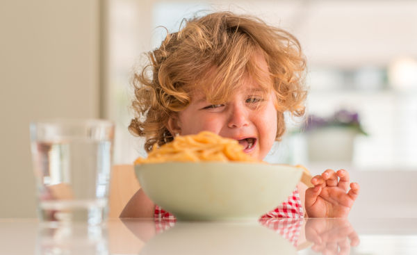 Beautiful blond child eating spaghetti with hands crying with ta