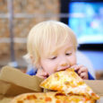 Cute Blonde Boy Eating Slice Of Pizza At Fast Food Restaurant
