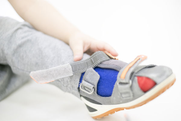 Small Child Tries To Put On His Shoes. Baby Boy With Shoes In Ha