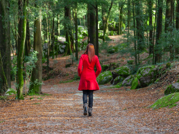 Young woman walking away alone on forest path wearing red long coat or overcoat.
