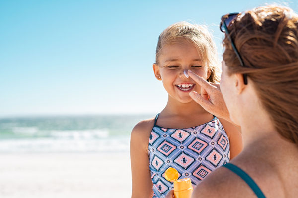 Young mother applying protective sunscreen on daughter nose at beach