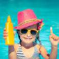 Happy child holding sunscreen lotion in hand. Summer vacations concept