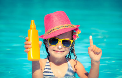 Happy child holding sunscreen lotion in hand. Summer vacations concept