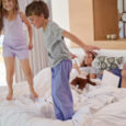 Happy children boy and girl siblings jumping on parents bed