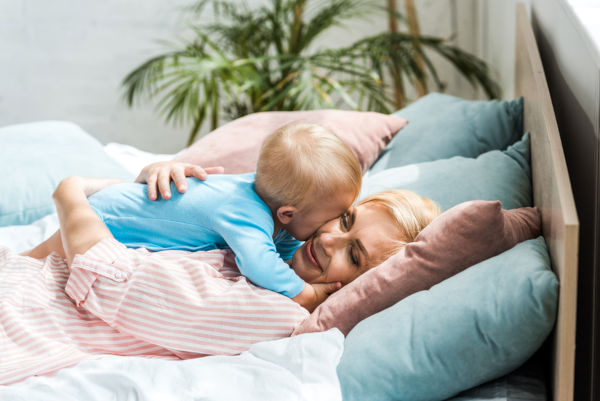 Mother Hugging Cute Toddler Son While Lying On Bed
