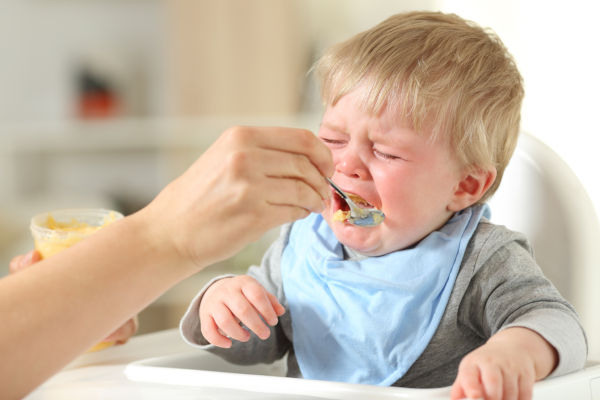 Toddler sitting in high chair and crying about food he is being fed