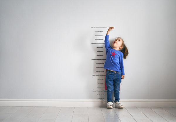 Child dressed as a superhero measuring herself on a height chart