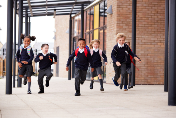 Primary school kids, wearing school uniforms and backpacks, running 