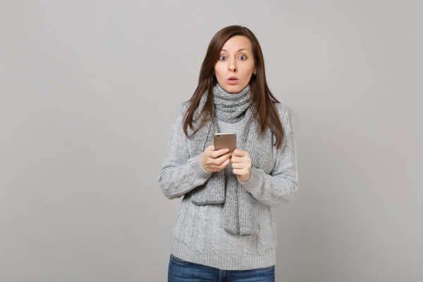 Woman in grey scarf looking surprised at phone messages