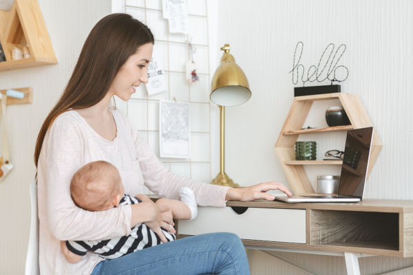 Woman holding sleeping baby whilst working on laptop